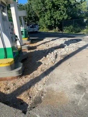 Saw-cut pavement and excavation beside a fuel dispenser.