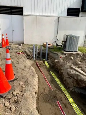 Utility trench with warning tape and partially covered service runs.