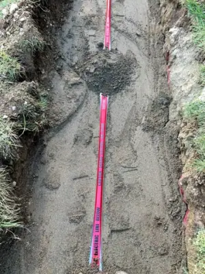 Partially backfilled utility trench with red warning tape.