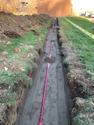 Partially backfilled utility trench with red warning tape.