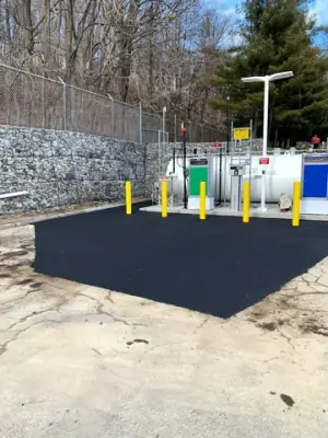 Fresh asphalt around the installed fueling equipment and protective bollards.