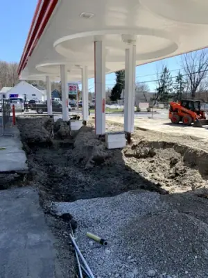 Excavated fueling-island area with open channels and earthmoving equipment.