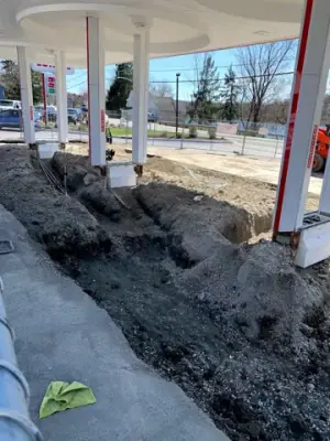 Excavated fueling-island area with open channels and earthmoving equipment.