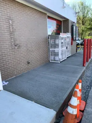 Finished sidewalk along the building with protective red posts.