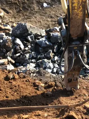 Excavator attachment working among fractured rock.