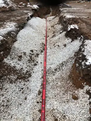 Aggregate backfill with red warning tape along the trench.