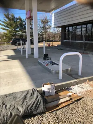 Concrete fueling island and protective rail beneath the canopy.