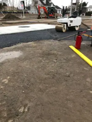 Paving roller compacting asphalt at the forecourt edge.