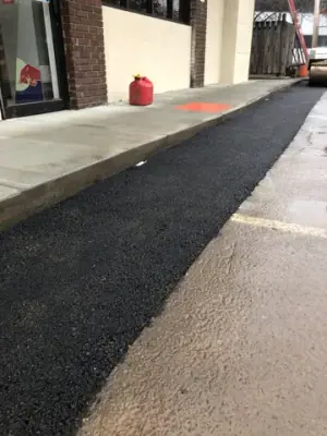 Fresh asphalt strip along the building-side walkway.