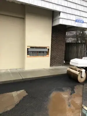 Wet ground and asphalt work beside the building entrance.